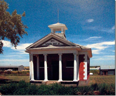 A color photo of a small brick school building with a front porch with ornate columns.