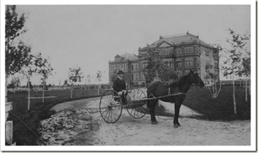 A black and white photo of a man sitting in a horse drawn buggy.