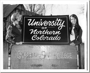 A black and white photo of two women standing being a sign that reads 