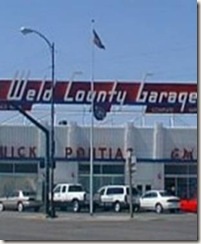 A color image of the Weld County Garage with several cars and trucks parked infront of it.
